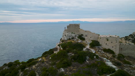 Drone-pullback---traveler-at-edge-of-Kastellos-ruins-overlooking-Aegean-Sea
