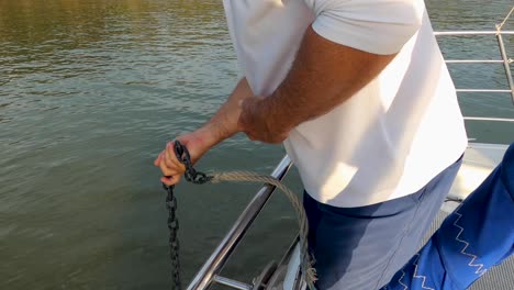 Closeup-of-man-letting-down-anchor-chain-with-his-hands-on-sailboat