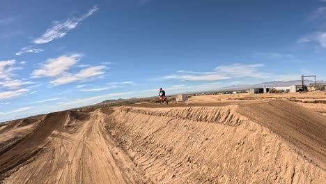 Following-a-motorcycle-racing-around-an-off-road-track-and-over-a-big-jump---first-person-view-drone
