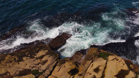 Top-view-pan-of-multiple-blue-green-white-ocean-waves-smashing-against-rocky-coastline-in-Australia