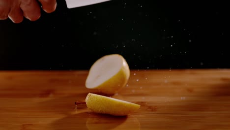 Sharp-knife-cutting-wet-pear-with-flying-water-drops-on-wooden-board,-super-slow-motion