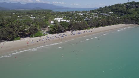 Beach-Umbrellas-On-The-Shore-At-Four-Mile-Beach-During-Summer-In-Port-Douglas,-Queensland,-Australia---aerial-pullback