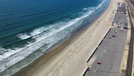 Aerial-over-Beach-Parking-Lot-on-Coronado-Silver-Strand-Beach-on-a-Warm-Summer-Day-2022-with-waves-and-people-laying-on-sand