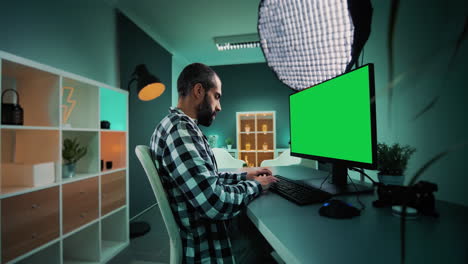 Young-freelancer,-copywriter,-designer,-editor-or-content-creator-working-on-desktop-computer-with-chroma-key-green-screen-mock-up-display