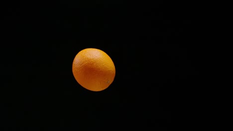 Fresh-delicious-orange-falling-down-in-slow-motion,-isolated-black-background
