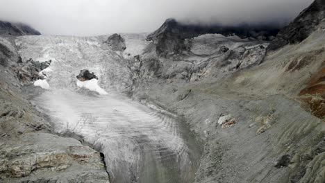 Fast-aerial-flyover-away-from-the-Moiry-glacier-near-Grimentz-in-Valais,-Switzerland-with-a-panoramic-view-of-the-ice-and-crevasses-on-an-overcast-summer-day
