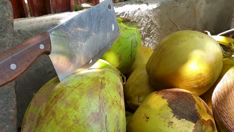 Piles-of-fresh,-healthy-and-delicious-coconuts-and-a-large-machete-to-open,-ready-to-drink-thirst-quenching-coconut-water,-on-a-remote-tropical-island-destination