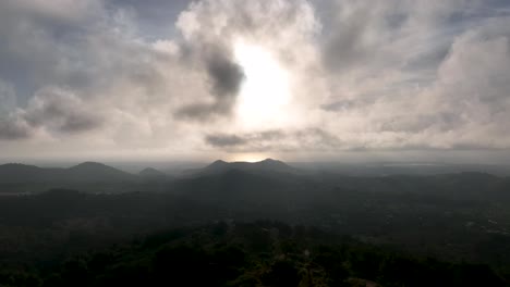 Aerial-of-sun-bursting-through-clouds-over-valley-with-mountains-and-sea