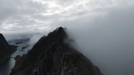 Flying-along-a-mountain-ridge-in-Norway,-on-the-right-no-view-through-fog-and-on-the-left-the-view-of-the-ocean-in-the-background,-in-slowmotion