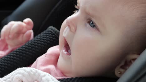 Baby-girl-sitting-in-car-seat-stares-straight-ahead-making-various-expressions