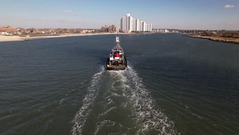 An-aerial-view-of-a-tugboat-on-a-sunny-day-in-the-East-Rockaway-Inlet-in-Queens,-NY