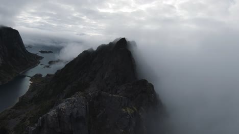 Flying-along-a-mountain-ridge-in-Norway,-on-the-right-no-view-through-fog-and-on-the-left-the-view-of-the-ocean-in-the-background