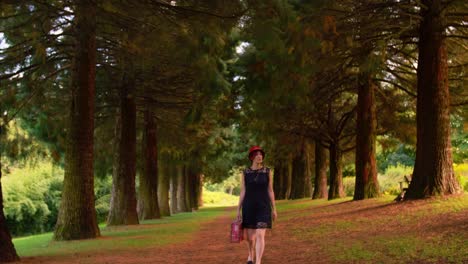 Smiling-young-woman-with-red-hat-and-black-dress-is-walking-towards-the-camera,-holding-a-red-vintage-suitcase-in-her-right-hand