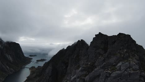 Flying-along-a-mountain-ridge-in-Norway,-on-the-right-no-view-through-fog-and-on-the-left-the-view-of-the-ocean-in-the-background