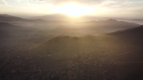 Neigende-Drohnenaufnahme-Eines-Orangefarbenen-Sonnenuntergangs-In-Den-Nebligen-Hügeln-Von-Lima,-Peru