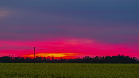 Dramatic-sunset-through-colorful-sky-with-green-field-in-the-foreground,-timelapse