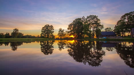 Reflective-lake-water-with-bright-sunset-behind-treeline,-fusion-time-lapse