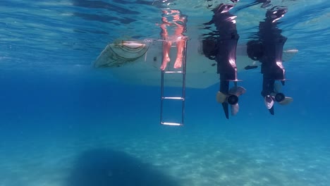 Slow-motion-under-water-tilt-up-shot-of-human-legs-and-feet-in-seawater-beneath-surface-protruding-from-double-engine-motorboat-ladder