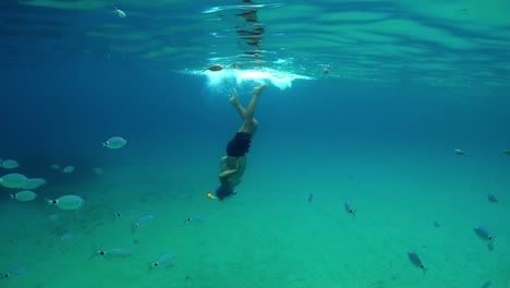 Slow-motion-underwater-scene-of-man-snorkeling-in-deep-blue-tropical-sea-water-with-school-of-fish-swimming-beneath-surface