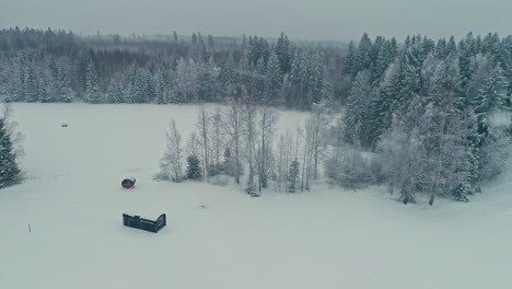A-lonely-cabin-in-a-cold,-winter-meadow-in-the-countryside---push-in-aerial-flyover-during-a-light-snowfall