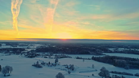 A-golden-sunset-on-the-horizon-over-a-winter,-snowy-landscape---descending-aerial-view