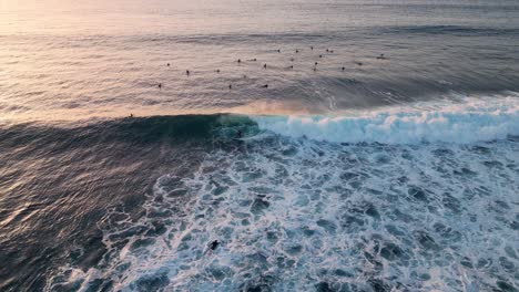 Aerial-view-of-a-surfer-catching-a-wave-at-sunset