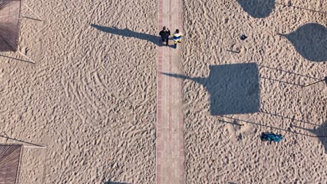Couple-walking-on-the-walkway-of-a-sandy-beach-in-autumn-on-a-sunny-day
