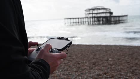 Fernbedienung-Mit-Telefon-Zum-Fliegen-Einer-Drohne,-Brighton-Beach,-Sussex