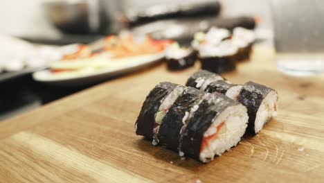 Person-Holding-With-Knife,-Green-Sushi-Roll-Slices-Side-By-Side,-Homemade-Preparation