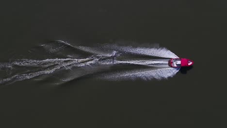 A-professional-water-skier-jumping-and-weaving-through-the-water-while-being-pulled-by-a-red-speedboat---Aerial-shot