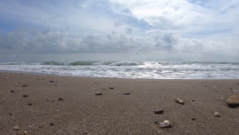 Sand-beach-with-sea-waves-and-foams,-blue-sky-with-white-clouds,-slow-motion-footage