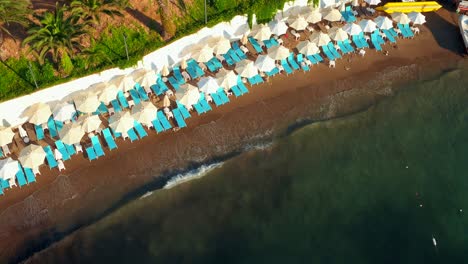 Drone-aerial-shot-of-waves-hitting-the-beach-full-of-umbrellas-and-sunbeds