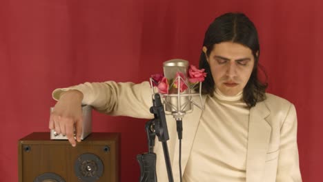 Man-In-The-Studio-Listening-To-The-Music-With-Eyes-Closed,-Red-Curtain-In-The-Background---Pink-Flowers-Around-A-Large-Diaphragm-Condenser-Microphone---medium-shot