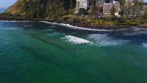 Surfers-Enjoying-The-Waves-At-The-Beach---Summer-Adventure-In-Burleigh-Head-National-Park---Beautiful-Place-In-Burleigh-Heads,-Queensland---aerial-drone,-panning-shot