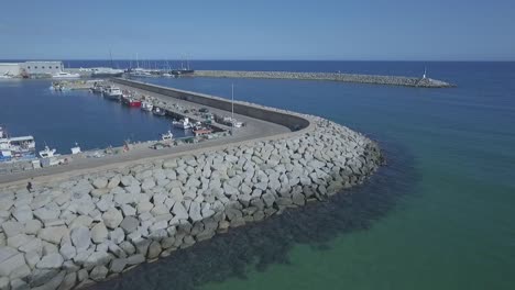 View-over-a-breakwater-construction-at-the-entrance-of-a-small-town-port,-aerial