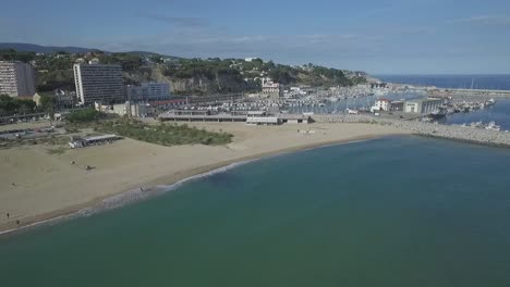 Coast-view-over-a-small-town-port-and-beach,-aerial-pull-away-shot