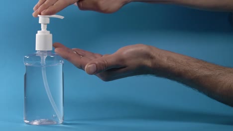 Using-antibacterial-hand-sanitizer-gel-against-blue-background,-slow-mo