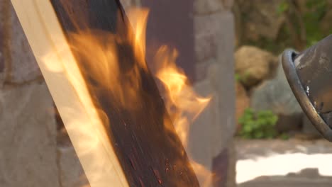 Propane-blowtorch-burning-pine-wood-plank-with-strong-flame,-closeup