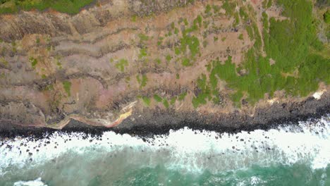 Waves-splashing-at-the-foot-of-Lennox-Head-Mountain-in-Australia--aerial