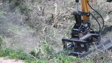 Close-up-shot-in-slow-motion-of-a-yellow-and-black-plant-machinery-arm-with-a-chain,-cutting-through-and-weeding-some-semi-dry-bushes-in-Spain
