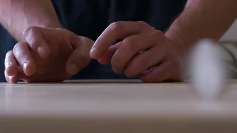 Skilled-man-hands-holding-coin-and-hitting-it-to-spin-and-bounce-along-wooden-table,-slow-motion-close-up-shot
