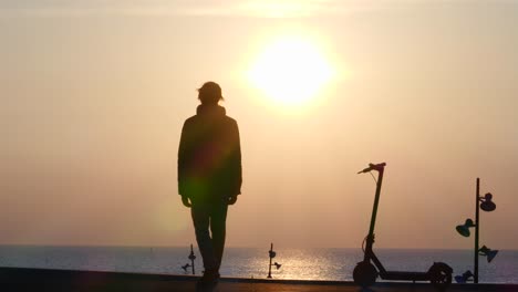 Silhouette-man-on-electric-scooter-stops-by-pink-ocean-sunrise-then-leaves