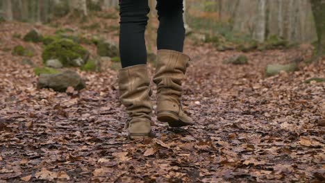 Low-angle-tracking-shot-of-woman-legs-walking-on-dry-leaves-carpet