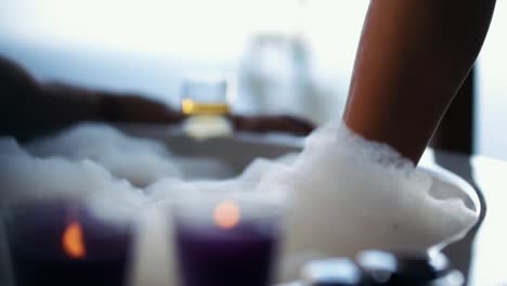Woman-dips-foot-into-a-bubble-bath-surrounded-with-purple-lit-candles