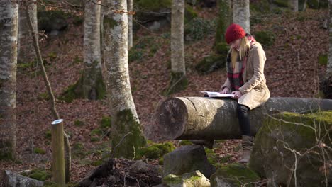 Woman-sitting-on-tree-trunk-relaxing-and-reading-book-in-woods