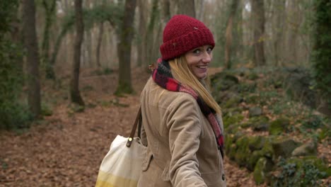 Young-woman-walks-in-woods,-turns-and-beckons-to-camera-to-follow-her
