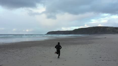 Carefree-Man-Enjoying-Running-With-Open-Arms-On-Beach-Of-Playa-de-Xago-At-Early-Morning-In-Asturias,-Spain