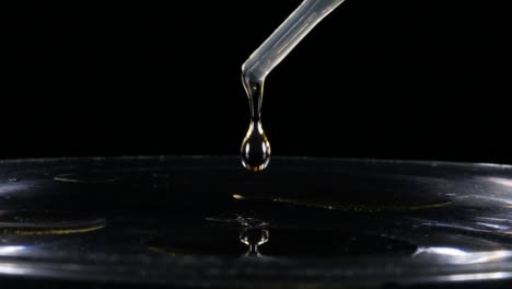 Pipette-dropper-pours-oil-in-water-on-black-background,-Slow-Motion-Closeup