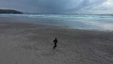 Single-man-run-on-an-empty-beach-then-have-a-break,-aerial-tracking-shot