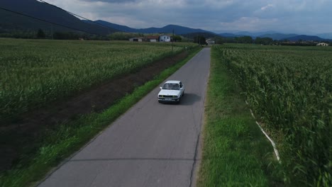 Bird's-eye-view-tracking-front-shot-of-a-car-driving-among-countryside-landscape